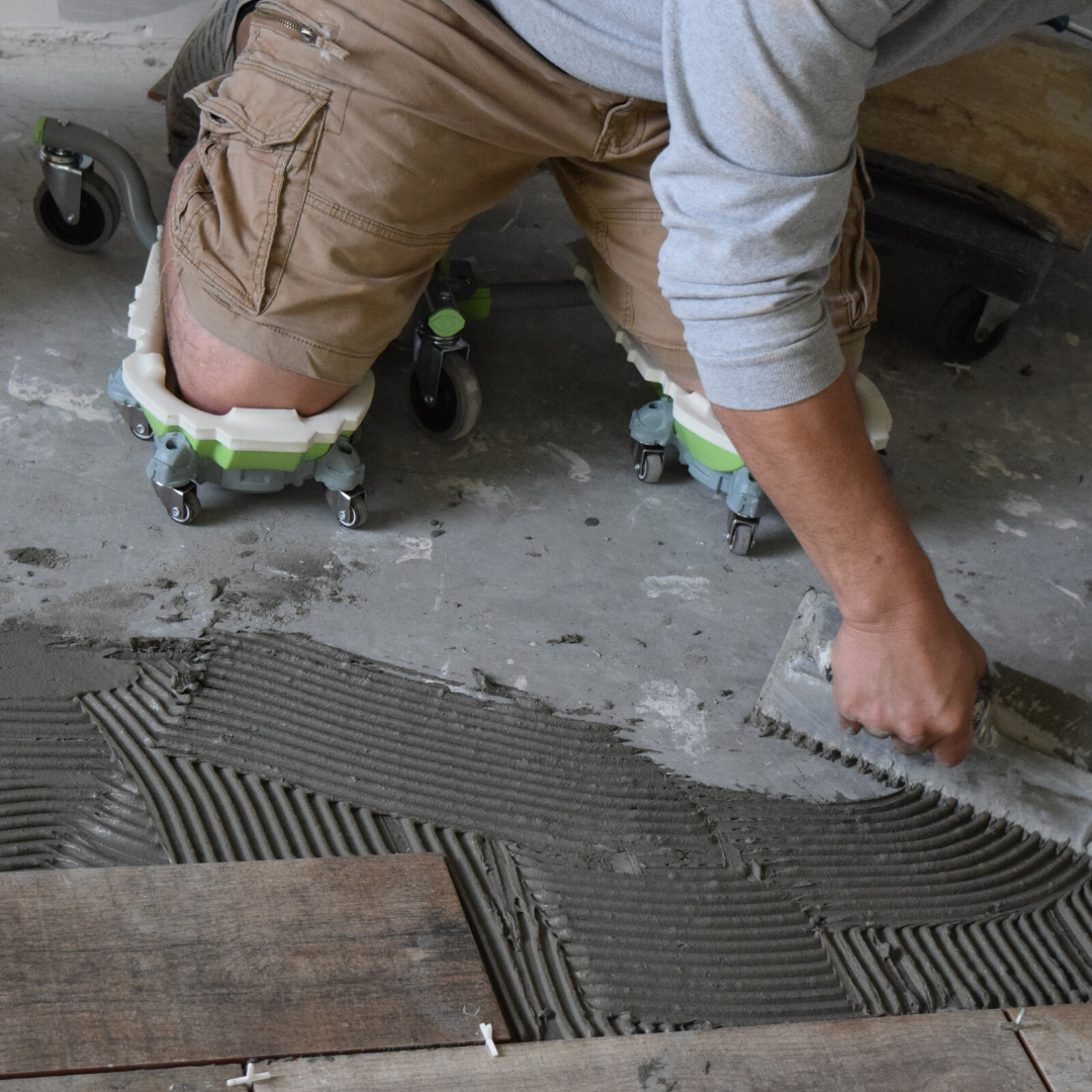 A man sits on the kneel-it as he lays down flooring at a job site.